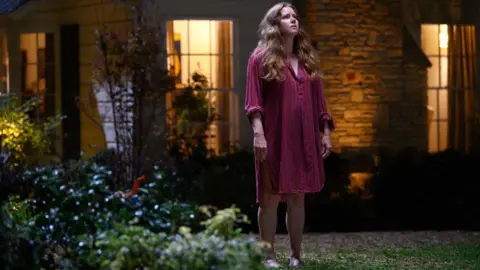 Searchlight Amy Adams in Nightbitch, pictured standing in the garden looking up at the sky
