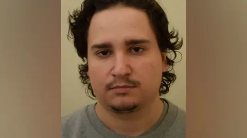 Counter Terrorism Policing South East and Regional Organised Crime Unit Gabriel Budasz' mug shot. He is wearing a grey shirt and has dark hair.
