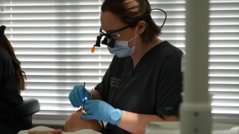 Shaun Whitmore/BBC Dr Alba Torrado-Varela is checking someone's teeth.