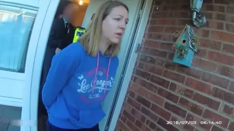 Cheshire Constabulary Police bodycam footage showing Letby, wearing a blue hoodie, being led from her the front door of a house with her hands behind her back.