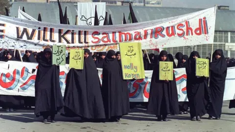 Getty Images Picture dated 17 February 1989 of Iranian women holding banners which read "Holly Koran" and "We will kill Salman Rushdie" during a demonstration in Tehran against the author of "The Satanic Verses". (Photo by NORBERT SCHILLER / AFP) (Photo by NORBERT SCHILLER/AFP via Getty Images)