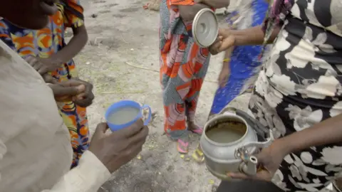 Women show pale grey water in a kettle and a cup in Roriak, South Sudan