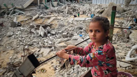 Anadolu via Getty Images A girl stands among the rubble of buildings destroyed by Israeli air strikes in in Khan Yunis, the Gaza Strip. Photo: 17 November 2024