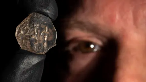 Crimestoppers/The Hunterian A close up of a bronze coin being held up by a man whose eye is visible in the background