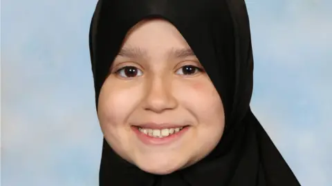 Surrey Police An image of Sara Sharif. She is wearing a hijab and is smiling, looking directly at the camera.