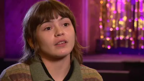 BBC Edie Kench-Andrews, general manager of the Moth Club, wearing a knitted shirt. She has brown, shoulder-length hair and a fringe.