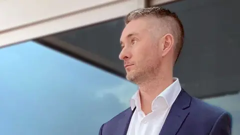 Richard Russell Man in a blue jacket and white shirt stares off into the distance. 