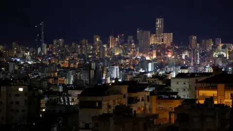 Reuters A nighttime view of Beirut’s illuminated cityscape, showcasing densely packed buildings and high-rise towers against the dark sky, after a ceasefire between Israel and Iran-backed group Hezbollah took effect at 02:00 GMT.