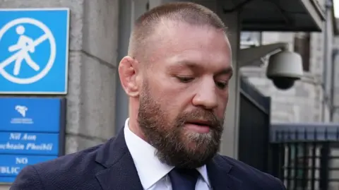 Brian Lawless/PA Wire Conor McGregor outside the High Court in Dublin. He has a beard, shaved hair and is wearing a navy suit and a white shirt.