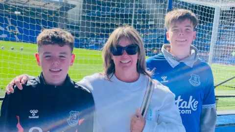 family handout Group family picture of Rita, flanked by her two sons in Everton shirts, by the Goodison Park pitch.