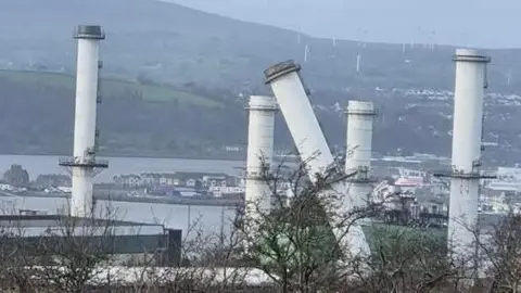 Maxine Johnston Ballylumford power station  - white chimneys, one is visibly damaged and bent, dwellings and mountains visible in background