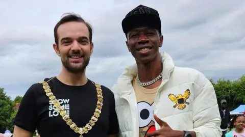 Beyond Skin Zambian rapper Smack Jay wearing a white jacket and black baseball cap stands alongside the Lord Mayor Micky Murray wearing a black t-shirt.