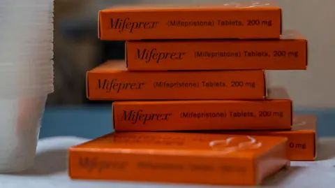 Evelyn Hockstein/Reuters A stack of orange tablet boxes on a table with Mifepristone labelled on them. They are next to a stack of clear plastic cups.