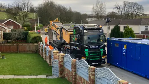 A conveyor lorry is parked on a residential street next to the sinkhole.