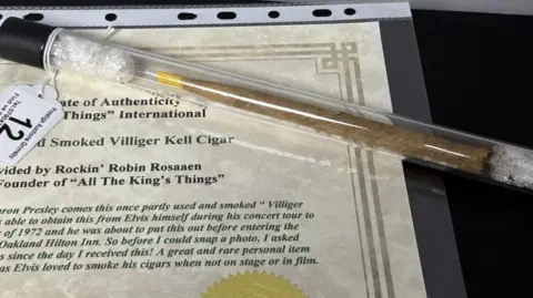 Prestige Auctions A long cigar with a yellow end concealed in a tube and resting on a certificate for the item.