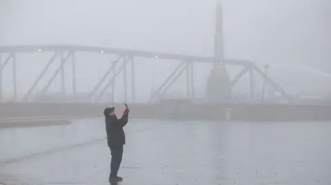 EPA A person takes photographs through thick fog at the Pier Head in Liverpool