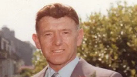 PA Media George Murdoch looking directly at the camera. He has dark eyes and brown hair and is wearing a grey suit with a light blue shirt.