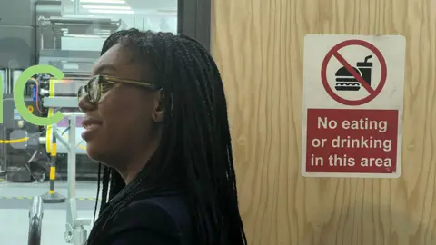 BBC Kemi Badenoch stands by a door with a sign reading: "Not eating or drinking in this area"