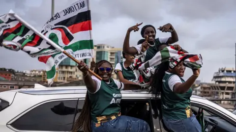 AFP Supporters of former Ghana President and presidential candidate for the National Democratic Congress (NDC), John Mahama (unseen) rise flags of NDC political party on they suit in a car during an electoral caravan ahead of presidential election of December 7, 2024, in Accra, on December 3, 2024.
