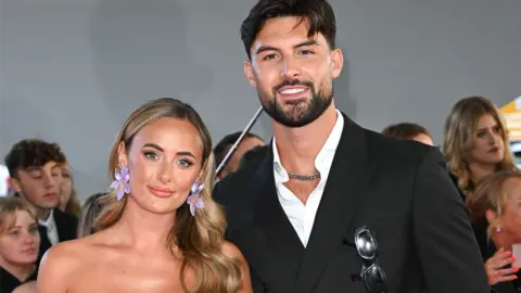 Getty Images Millie Court and Liam Reardon smiling at the camera, at an event with crowds of people behind them