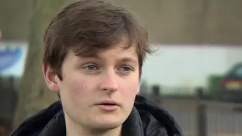 BBC Isaac, who has brown hair with a fringe and is wearing a hooded black coat and a dark green jumper, is pictured in a park