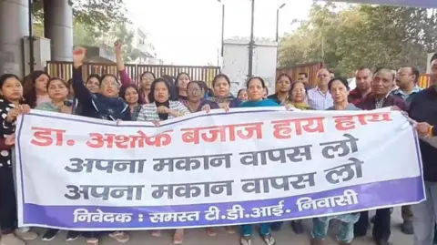Anoop Mishra Protesting residents seen holding a banner that calls for Dr Ashok Bajaj to take back the sale of his house