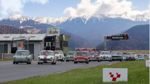 Senna/Causeway Pictures Images of cars on a race circuit with the sign Snetterton above the track, with a range of snow-capped mountains in the background. 