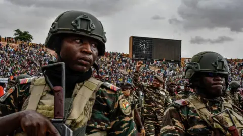 AFP Flanked by troops, Niger's coup leader Gen Abdourahamane Tchiani (C) greets the thousands of people at a stadium in Niamey on 26 July 2023. They are all wearing camouflage.