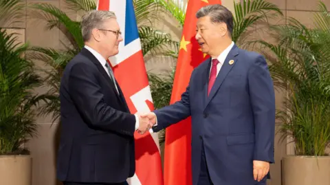 PA Media Prime Minister Sir Keir Starmer shaking hands with President Xi Jinping in front of a British and Chinese flag.