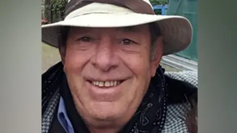 Family Photo Kelvin Evans, pictured smiling and wearing a beige brimmed hat. He has a checked jacket on.