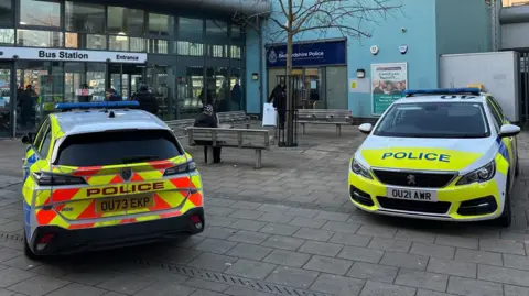 Kimberley Piper/BBC Two police cars parked on the pavement outside Bedford bus station. There is a police station next to the bus station, and the entrance to the police station is in the shot.