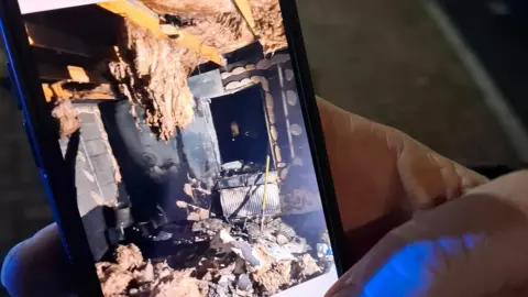 Chloe Taylor A hand holds a mobile photos showing photos of extreme fire damage to Chloe Taylor's home. 
