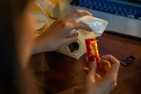 Fritz Pinnow Sometimes clients who send in their film rolls also send sweets an little notes. Lucia holds up one of the sweets that came in one of the small packages sent by client.