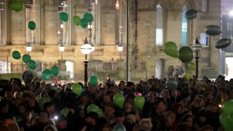 Reuters Image shows people holding green balloons during a vigil for James Lee Williams, popularly known as The Vivienne, in Liverpool on 12 January, 2025