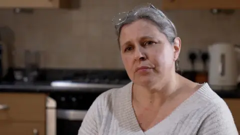 A woman with grey, glasses on her head and a v-neck light grey sweater