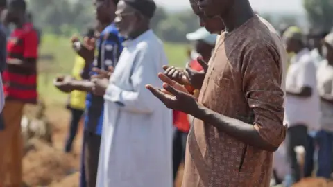 Ifiokabasi Ettang / BBC Male Muslim mourners hold up their hands in prayer as they attend a funeral at Tudun Wada cemetery