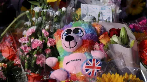 PA Media A colourful teddy which has 'Southport' on its belly nestled in flowers