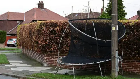 Getty Images A damaged trampoline which has been blown out of a garden during a storm and is now caught between a hedge and an electricity pole.