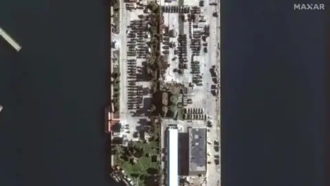 Maxar Military vehicles at Tartous port on 17 December. They are parked in rows with greenery buildings surrounding them.