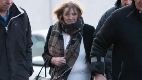 Athena Picture Agency Bridget Curtis who has fair hair and is wearing a white top, black jacket and black-and-brown scarf