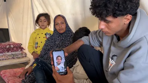 Family members in a tent show pictures of Aya on a mobile phone