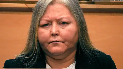 Firecrest\BBC Photo of Donna Brand in court. She has long hair which is going grey and is wearing a black jacket.