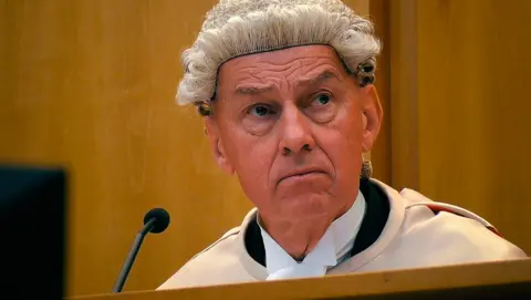 Firecrest Films/BBC Photo of the judge in court. He is wearing his court robes and wig. He is sitting in front of a microphone and looking towards the court.