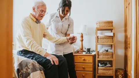 Getty Images nurse helps a man up from sitting down