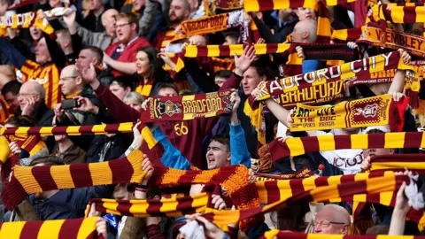 Getty Images A crowd of Bradford City football fans holding claret and amber striped scarves in the air.