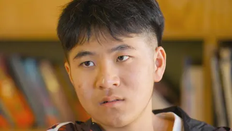 BBC Zhang Junjie speaking to the BBC indoors - he gazes intently at the reporter and is dressed casually. He has short brown hair, slightly shaved at the sides.