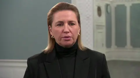 Reuters Denmark's prime minister sits, staring at a camera, wearing a dark jacket and earrings