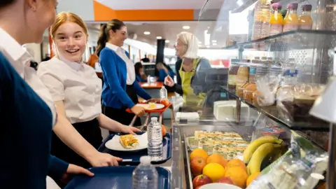 Getty Images Three schoolgirls queuing to pay for their school meals. There are number of healthy options on glass shelves in front of them, including a selection of fruit.