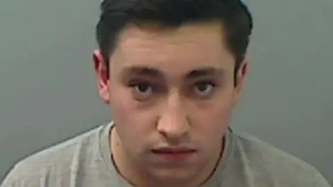 Cleveland Police Mugshot of Dismore. He is clean shaven and has dark hair, and is wearing a grey sweatshirt