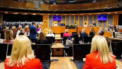 Reuters A general view of the Senedd during a royal visit, with the King and Queen Camilla sat in the centre, and a harp in view. Vaughan Gething, who was first minister at the time, is stood with his back to the camera.